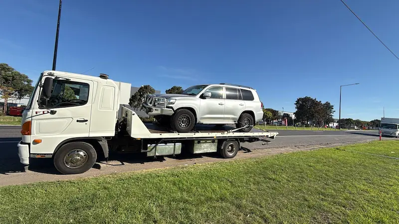 White tilt tray tow truck transporting a silver Toyota LandCruiser 4WD for cash in Ballarat City Centre.